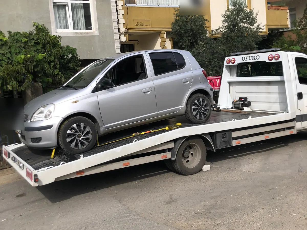 Gümüş hatchback aracın kayışla sabitlenip çekiciye yüklenmesi